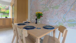 A dining table set with blue coasters, wine glasses, and a bottle of wine, with a map on the wall behind. - Heathercroft Apartment-Modern Comfort in Fort William. (Fort William)