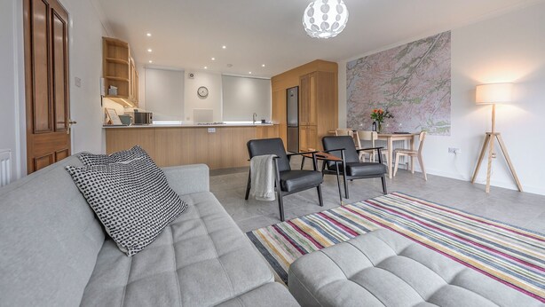 A modern living room with a grey sofa, a striped rug, and a dining area with chairs and a table. - Heathercroft Apartment-Modern Comfort in Fort William. (Fort William)