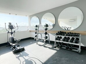 Ginásio com equipamentos de exercício, incluindo esteira, banco de musculação e halteres.