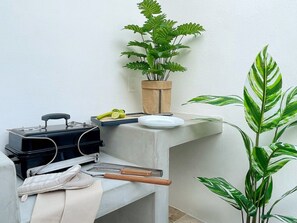Een hoek van een kamer met een plant in pot, een zwarte koffer en een bank met een witte doek.