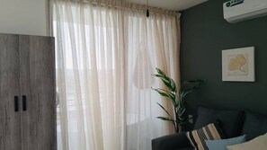 Quarto com uma grande janela, uma planta, um sofá e um ar-condicionado fixado na parede.