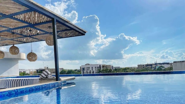 Une piscine avec un bord carrelé, un espace de repos couvert avec des chaises, et un ciel dégagé.