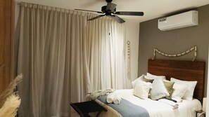 Une chambre à coucher avec un lit, un ventilateur de plafond, un appareil de climatisation et une fenêtre avec des rideaux.
