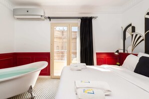 Relax in a classic room with a large bed, white bathtub, and air conditioning unit, offering a view of the building's exterior.