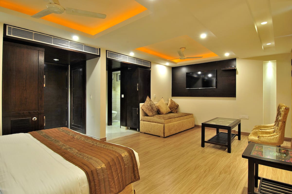 A modern hotel room with a bed, a sofa, a TV, and a desk.