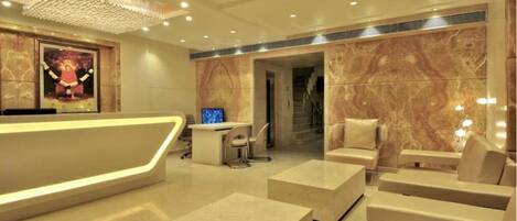 A modern hotel lobby with a reception desk, seating area, and a staircase leading to other floors.