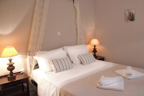 A neatly made bed with white linens and striped pillows, two bedside lamps, and a small painting on the wall.