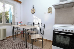 A kitchen with a dining table, chairs, a stove, and a window with lace curtains.