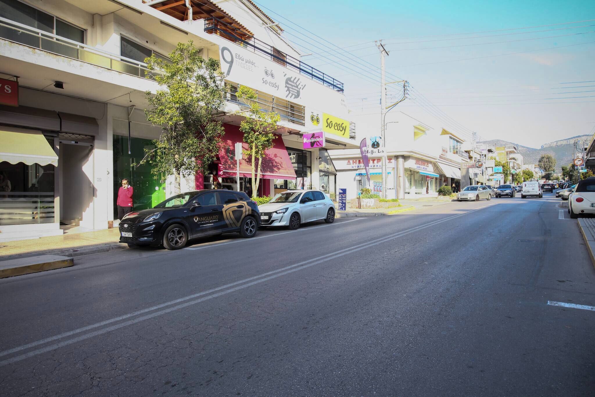 A street with cars parked on the side, buildings with various signs, and a clear sky.