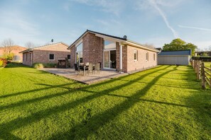 Une maison de plain-pied en briques, dotée d’une terrasse, d’un garage et d’une cour clôturée.