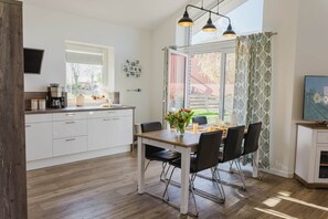 Une cuisine moderne avec des meubles blancs, une table à manger en bois, des chaises noires et une fenêtre avec des rideaux.