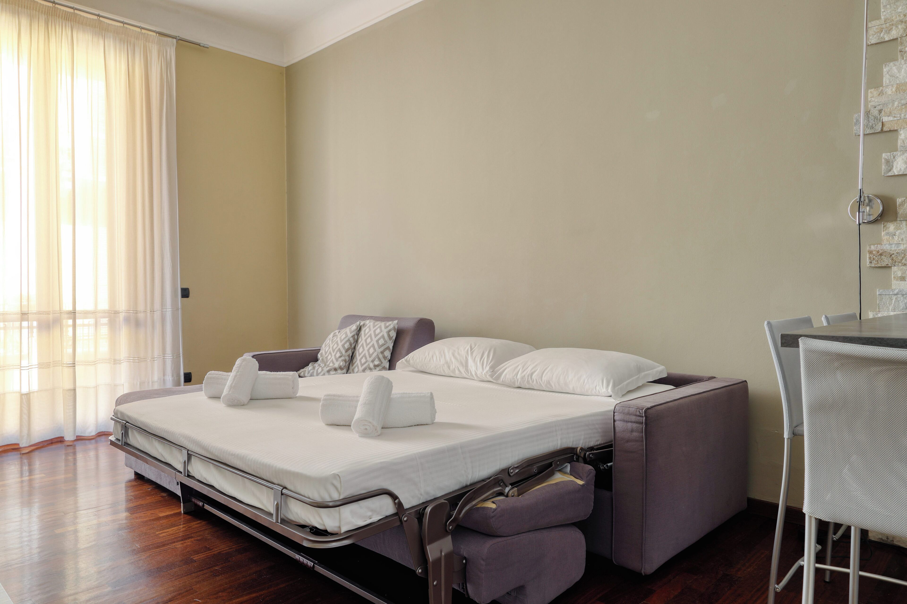 A modern hotel room with a convertible bed, a small table, and a chair.