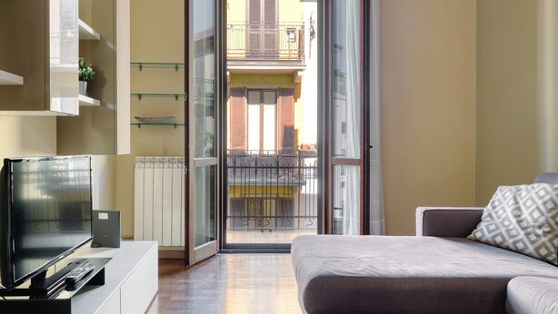 A modern living room with a flat-screen TV, a sofa, and a sliding glass door leading to a balcony.