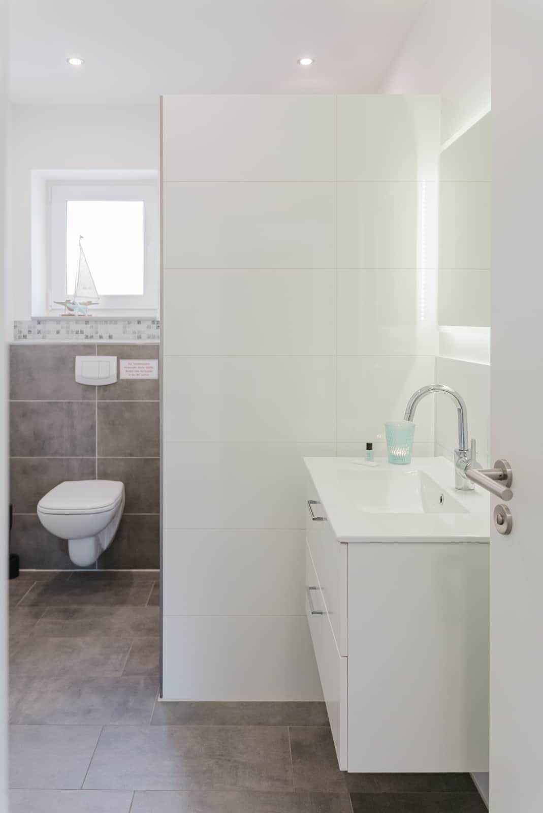 A modern bathroom with a white sink, mirror, and toilet.