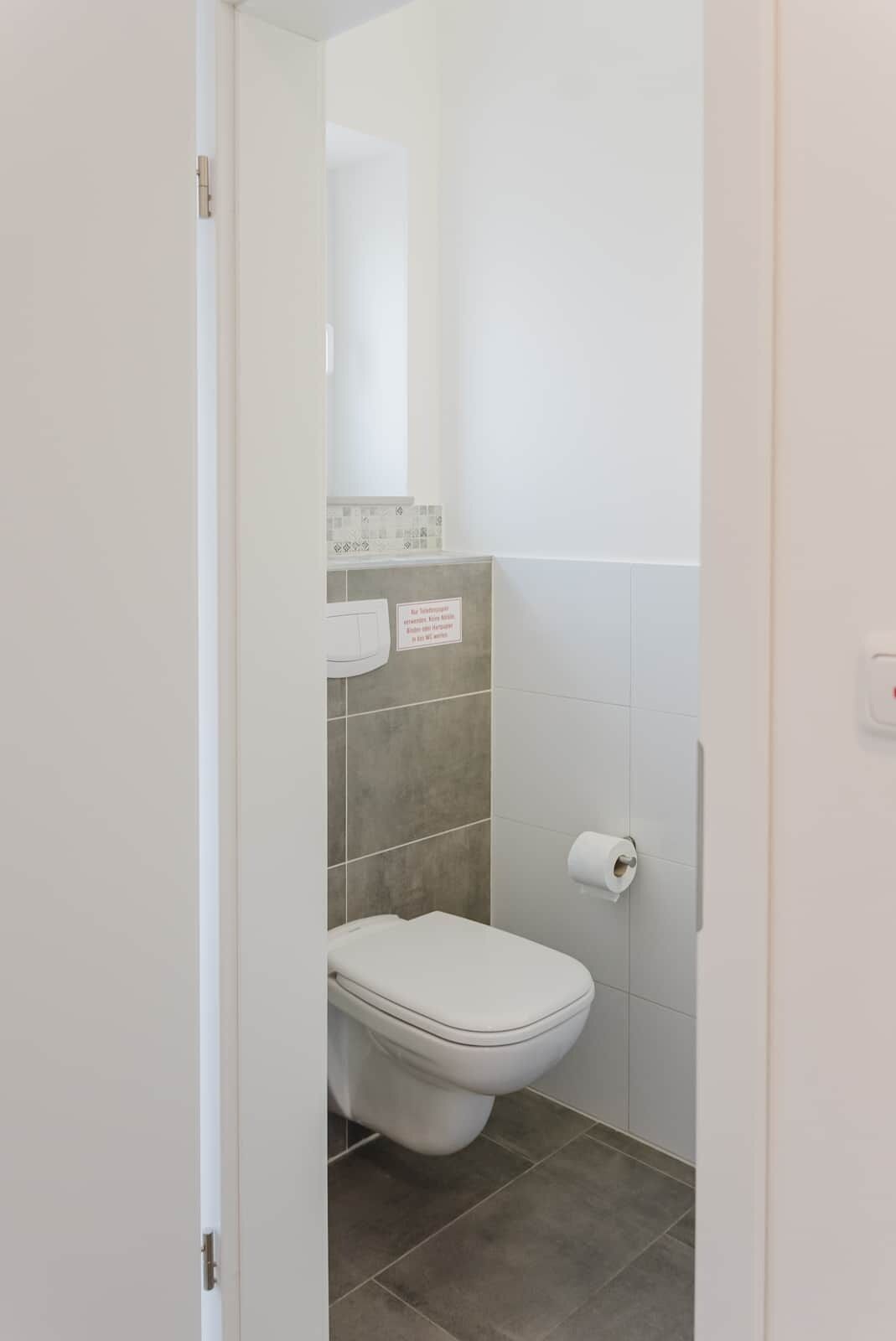 Une petite salle de bain propre, équipée de toilettes, d’un distributeur de serviettes et d’un porte-rouleau de papier toilette.