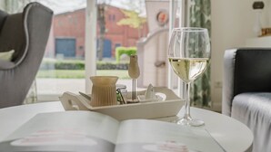 Una habitación con una mesa dispuesta para una comida, una copa de vino blanco y vistas a un edificio.