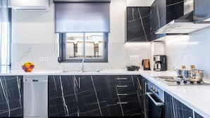 Een moderne keuken met zwarte marmeren aanrechtbladen, een vaatwasser, een spoelbak en een raam met uitzicht op gebouwen.