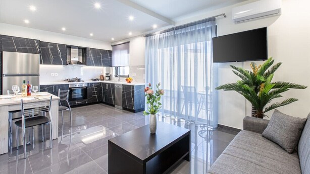 Een moderne keuken met donkere marmeren werkbladen, roestvrijstalen apparatuur, en een eethoek met een glazen tafel en stoelen.