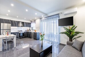 Une cuisine moderne avec des plans de travail en marbre foncé, des appareils électroménagers en acier inoxydable et un coin repas doté d’une table et de chaises en verre.