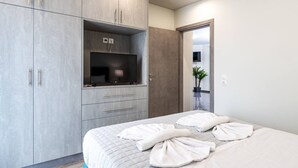 Een moderne slaapkamer met een bed, een aan een kast bevestigde televisie en een deur die naar een andere kamer leidt.