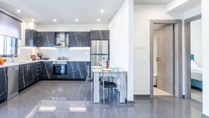 Een moderne keuken met donkere marmeren aanrechtbladen, roestvrijstalen apparatuur en een eethoek met een glazen tafel en stoelen.