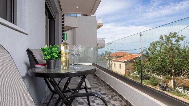 Un balcone con un tavolo, due bicchieri, una bottiglia e un vaso con una pianta.