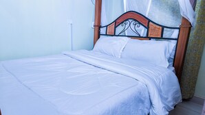 A bed with a wooden headboard, white bedding, and a plain wall. - Zedek Suites (Nairobi)