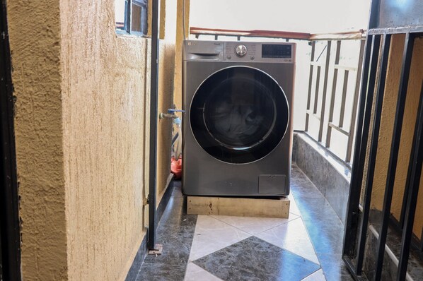 A washing machine in a narrow hallway with tiled flooring and a metal railing. - Zedek Suites (Nairobi)