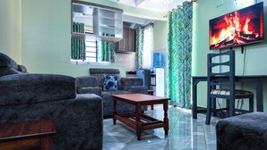 A living room with a sofa, a coffee table, and a TV displaying a fire. - Zedek Suites (Nairobi)