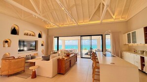 Amplia sala de estar con televisor grande, asientos cómodos, una mesa de comedor y vista al océano.