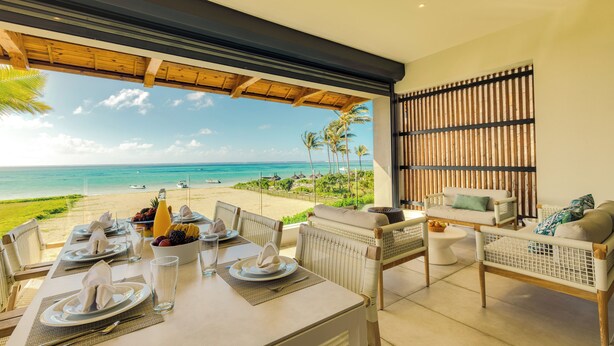 Un comedor con una mesa dispuesta para dos personas, con vista a una playa con palmeras y el océano.