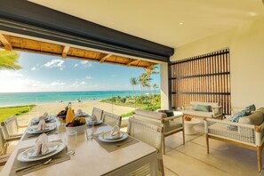 Un comedor con una mesa dispuesta para dos personas, con vista a una playa con palmeras y el océano.