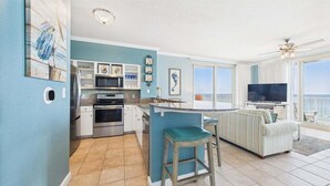 Una cocina moderna con una isla central, un comedor con sofás a rayas y un televisor grande.