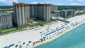 Un hotel costero con varios edificios altos, una playa con numerosos paraguas y una vista despejada del océano.
