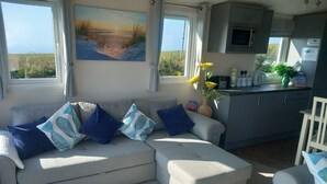 A modern living room with a grey sofa, blue cushions, and a painting of a beach scene. - Valley View -panoramic views of Rame Peninsula (Torpoint)