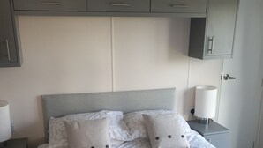 A bedroom with a bed, two nightstands, a bedside lamp, and grey cabinets above the bed. - Valley View -panoramic views of Rame Peninsula (Torpoint)