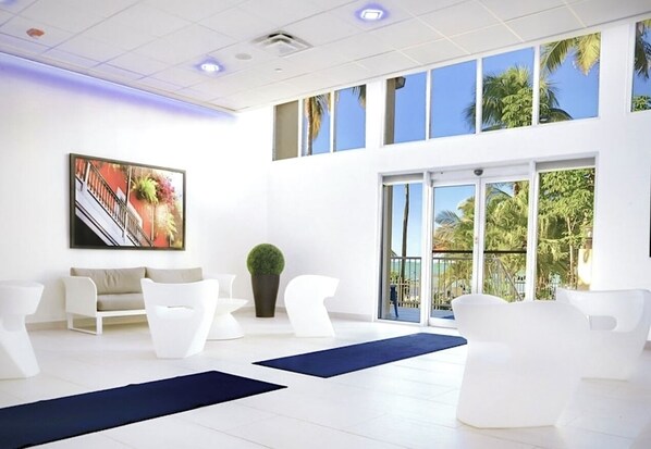 Un moderno vestíbulo de hotel con mobiliario blanco, un cuadro grande y vistas a palmeras a través de las ventanas.