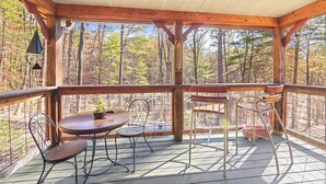 Une terrasse en bois avec une table et des chaises, entourée d’une rambarde en métal, donnant sur une forêt.