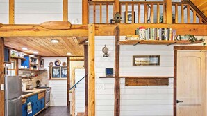L’intérieur d’un chalet rustique comprend un escalier en bois, un coin cuisine et un espace salon confortable avec un canapé en cuir et une petite table ronde.