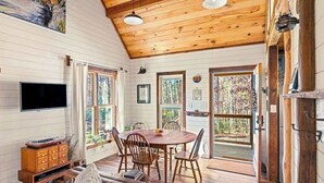 L’intérieur chaleureux d’un chalet avec une table à manger en bois, des chaises, un canapé et un téléviseur.