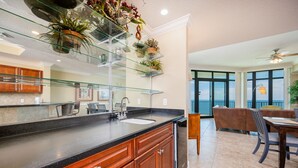 Una cocina moderna con repisas de vidrio, armarios de madera y un comedor con mesa y sillas.
