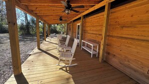 Eine Holzterrasse mit Deckenventilatoren, weißen Schaukelstühlen und einer Bank.