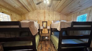 Ein Holzhütten-Interieur mit Holzwänden und -böden, Etagenbetten, einem Nachttisch mit Lampe und einem Fenster.