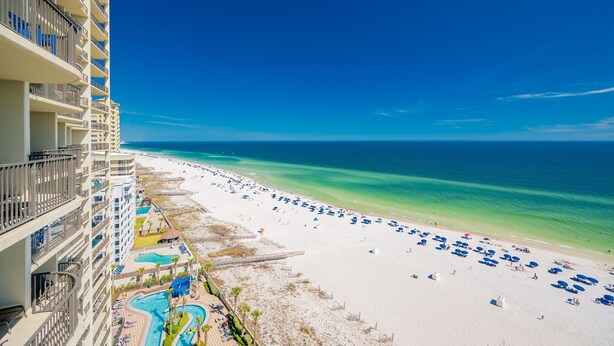 A beachfront hotel with a pool, beach umbrellas, and a clear view of the ocean.