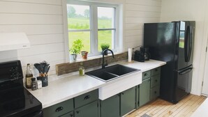 Una cocina con un refrigerador negro, un lavamanos y una ventana con vistas a un campo verde.