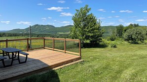 Una terraza de madera con mesas de picnic que da a un campo cubierto de hierba y colinas a lo lejos.