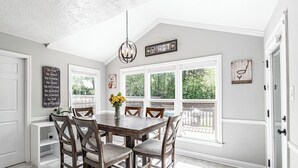 A dining area with a wooden table and chairs, large windows, and a view of greenery outside. - Spacious Master's Rental w/Pool in the Heart of Evans (Evans)