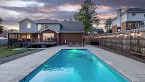 A rectangular swimming pool with a wooden deck surrounding it, a covered patio area, and a wooden fence. - Spacious Master's Rental w/Pool in the Heart of Evans (Evans)