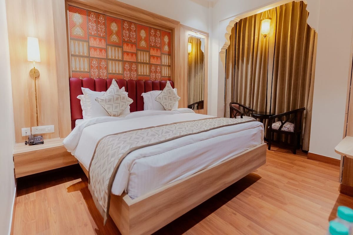 A hotel room with a large bed, a wooden headboard, a bedside table with a lamp, and a chair by the window.