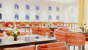 A modern restaurant with orange upholstered chairs, white tables, and blue decorative elements on the walls. - Hotel Ratan Mahal (Datia)